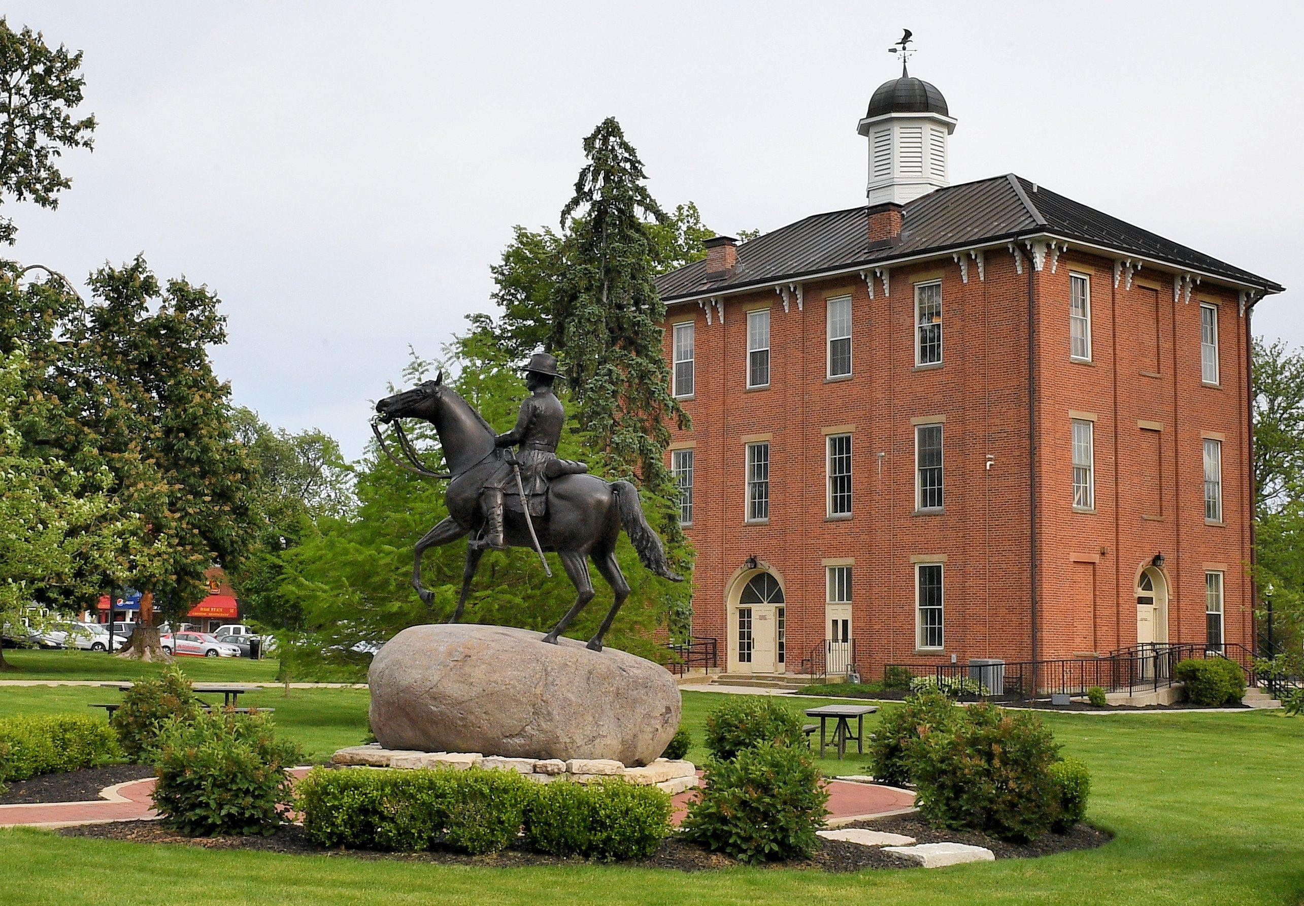 An outside view of town hall with a statue of a man on a horse and grounds